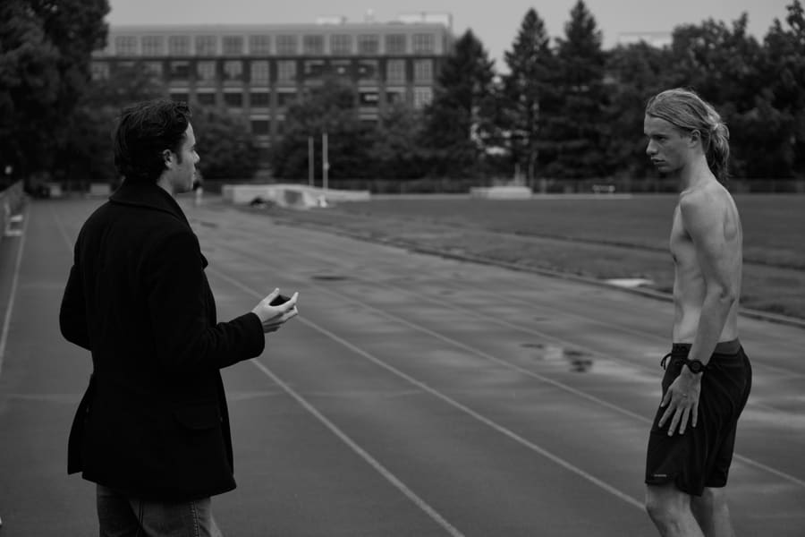 A coach holding a stopwatch talks with a runner on an outdoor track