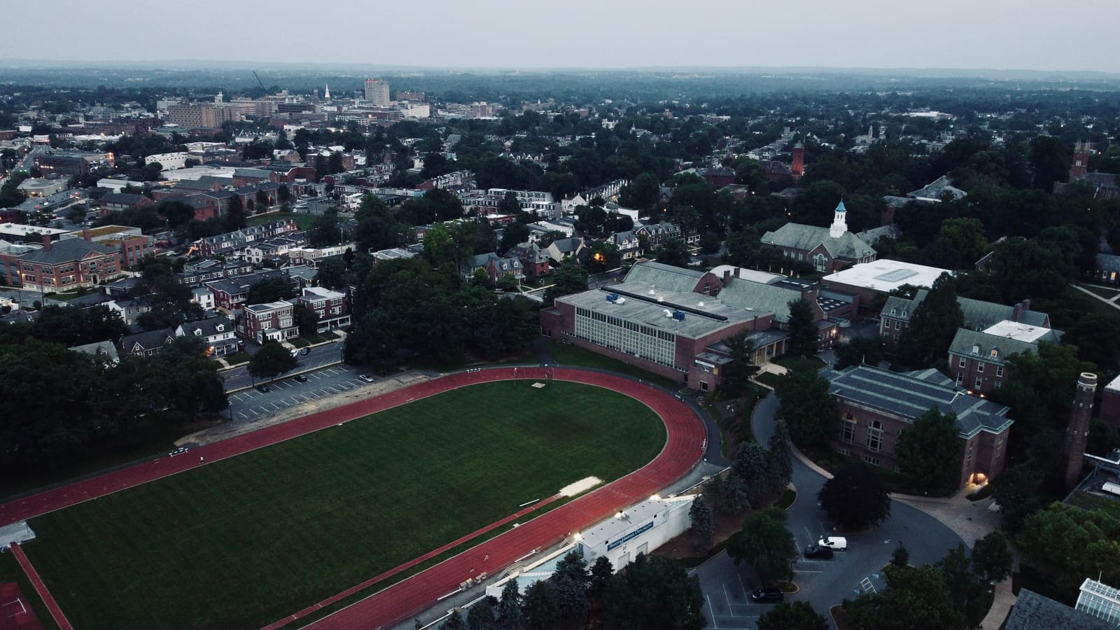 Aerial view of an outdoor running track and the city beyond at dusk